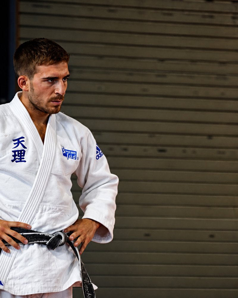Kevin en kimono de judo, mains sur les hanches, dans une salle d'entraînement